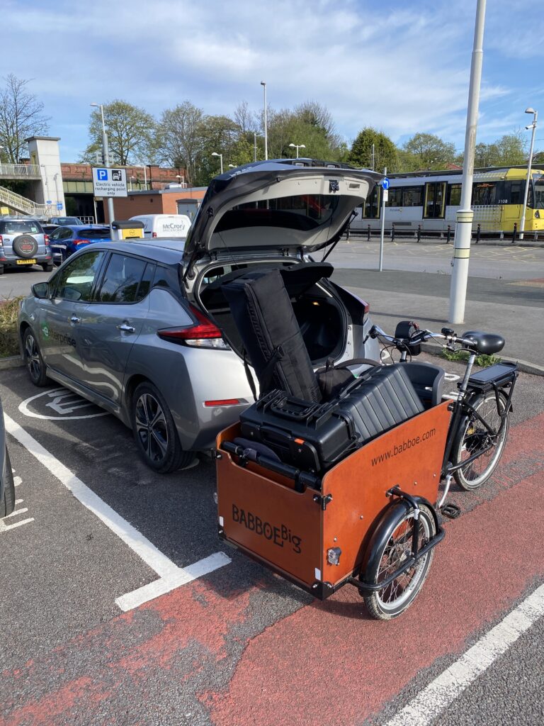 A cargo bike filled with camera equipment, being loaded into the boot of an electric car.