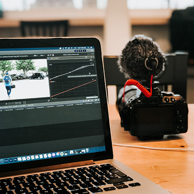 A laptop with editing software open, next to a video camera with a microphone on top