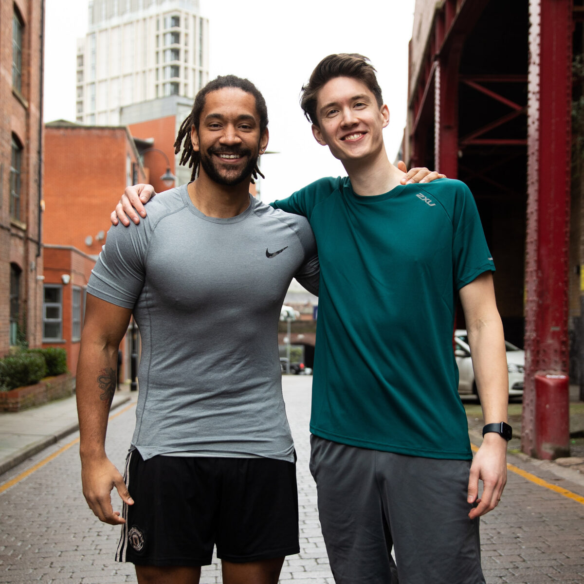 Two men standing on a street wearing running clothes, with their arms around each other.