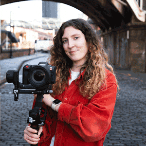 Animated GIF of a woman holding video camera on a gimbal, on a cobbled street