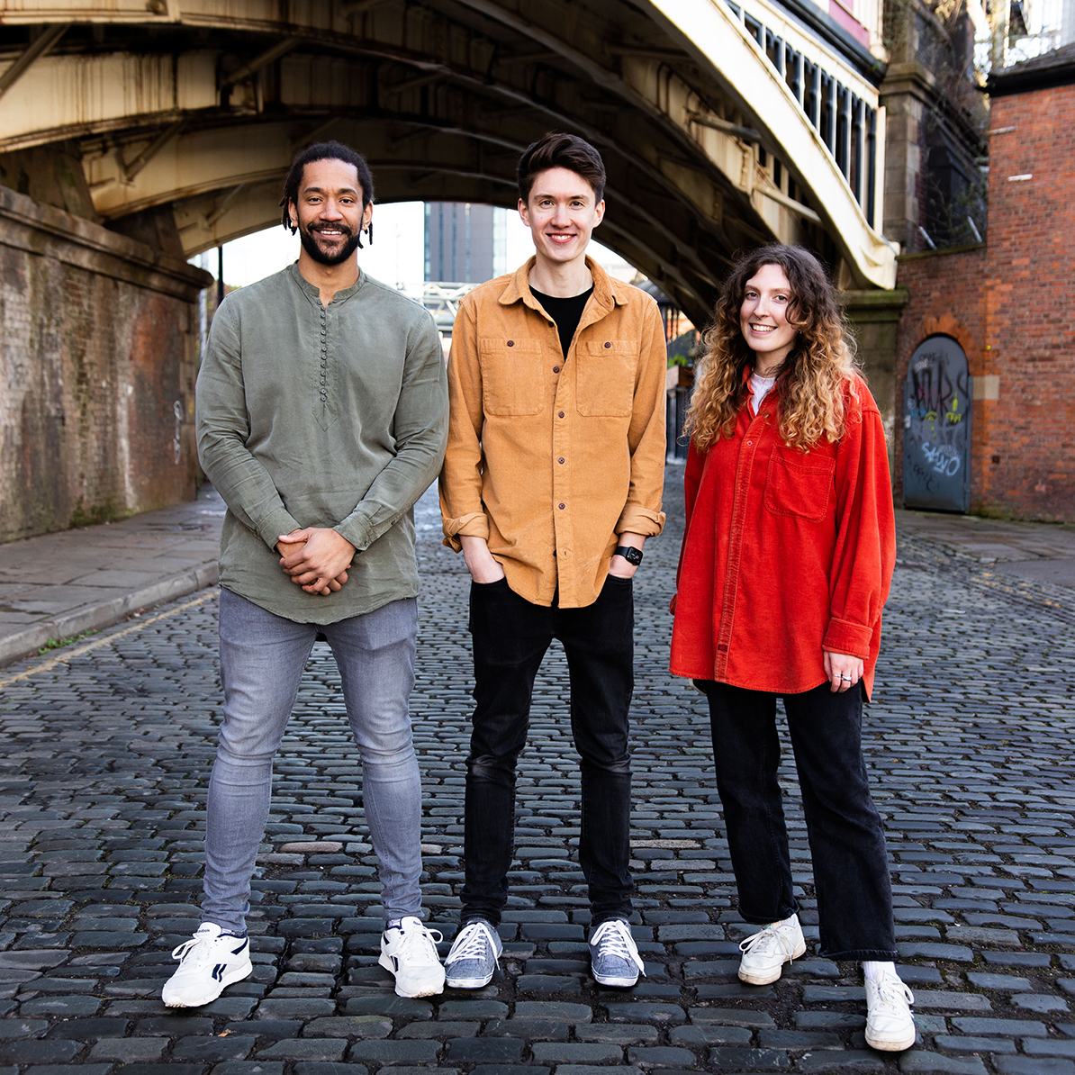 Three people standing together in the middle of a cobbled city street