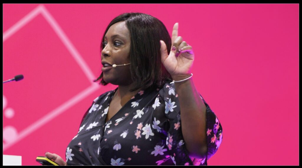 A woman speaks on stage at an event. Reformatted to show more space on the right of the frame.