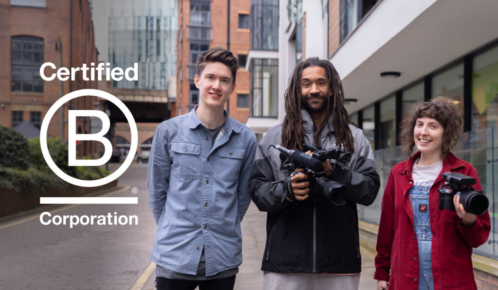 Three people standing on a street, smiling, two of them holding video cameras. Logo overlaid on the left says Certified B Corporation.