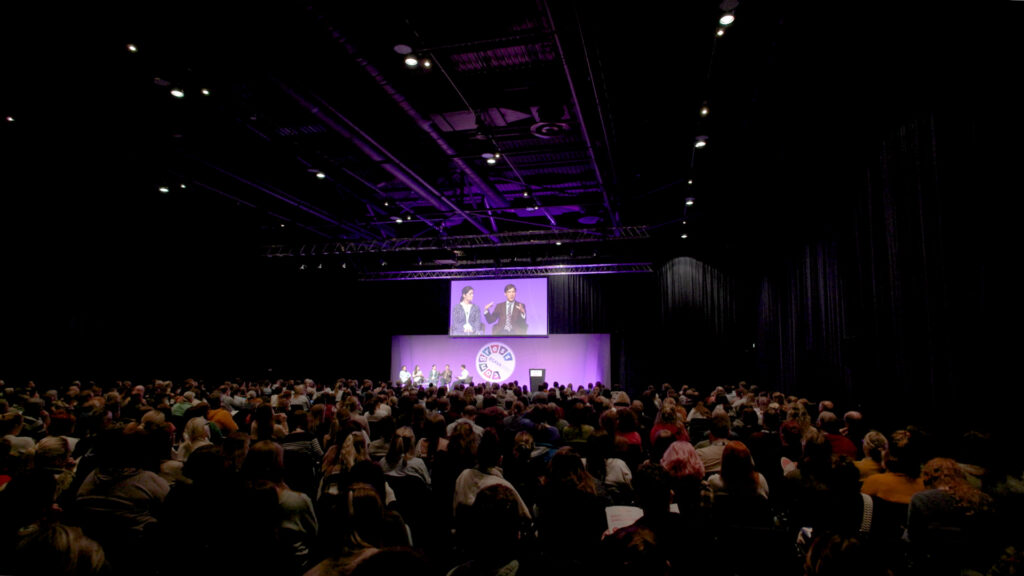 Screengrab of event videography showing a large audience watching a speaker on stage