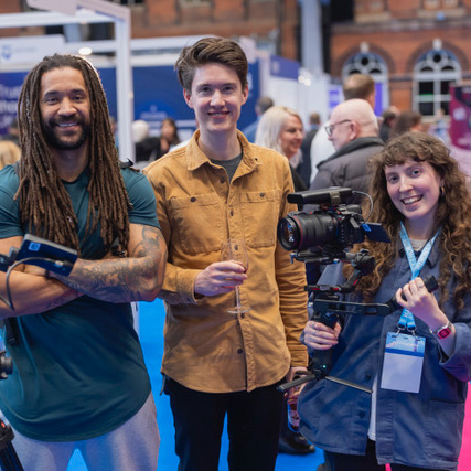 Jamie, Ben and Natalie from Studio 91 Media, standing together and smiling with camera equipment at the HETT North conference at Manchester Central